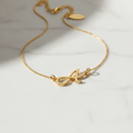 Colar Inicial Personalizada - semijoia dourada com pingente de letra inicial cursiva sobre mesa branca